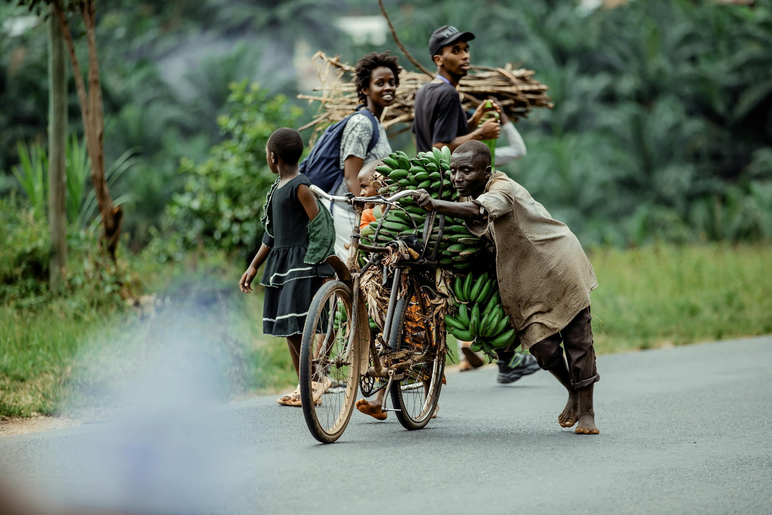 African villagers transport bananas and firewood on a rural road, showcasing daily life.