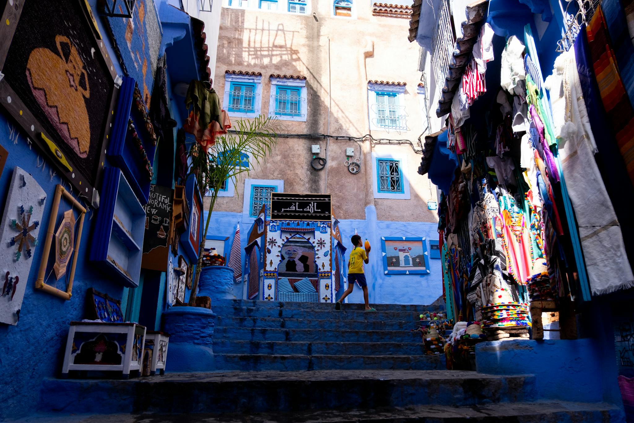 Child playing in a colorful alleyway in Chefchaouen, showcasing street art and textiles.