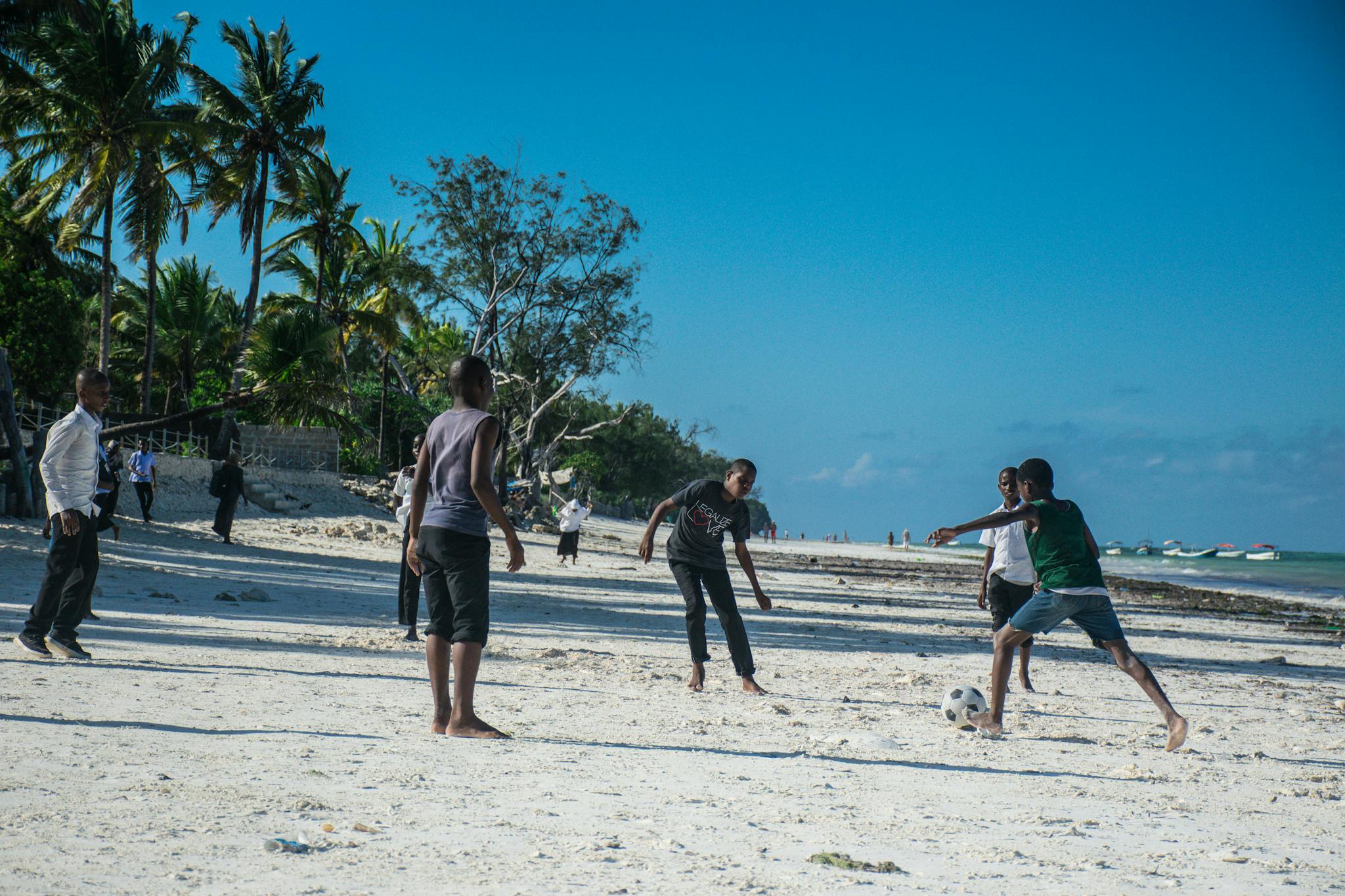 Group of boys enjoying a lively soccer game on a sunny Zanzibar beach.